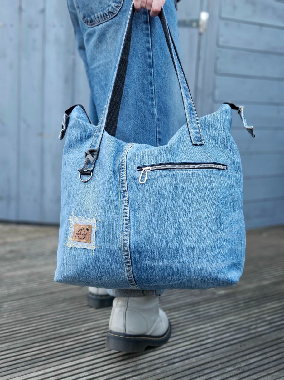 Light Denim Tote Bag Light blue denim tote bag worn on the shoulder with long handles, double zipper closure and front zip pocket.