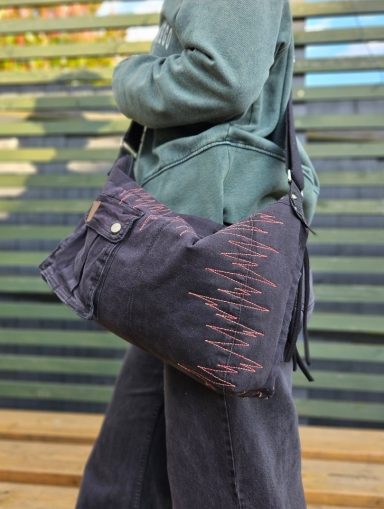 black denim crossbody bag with red stitching worn on shoulder