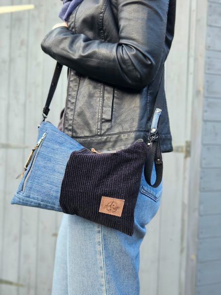 Small denim crossbody bag worn on shoulder with dark corduroy panel and compact shape