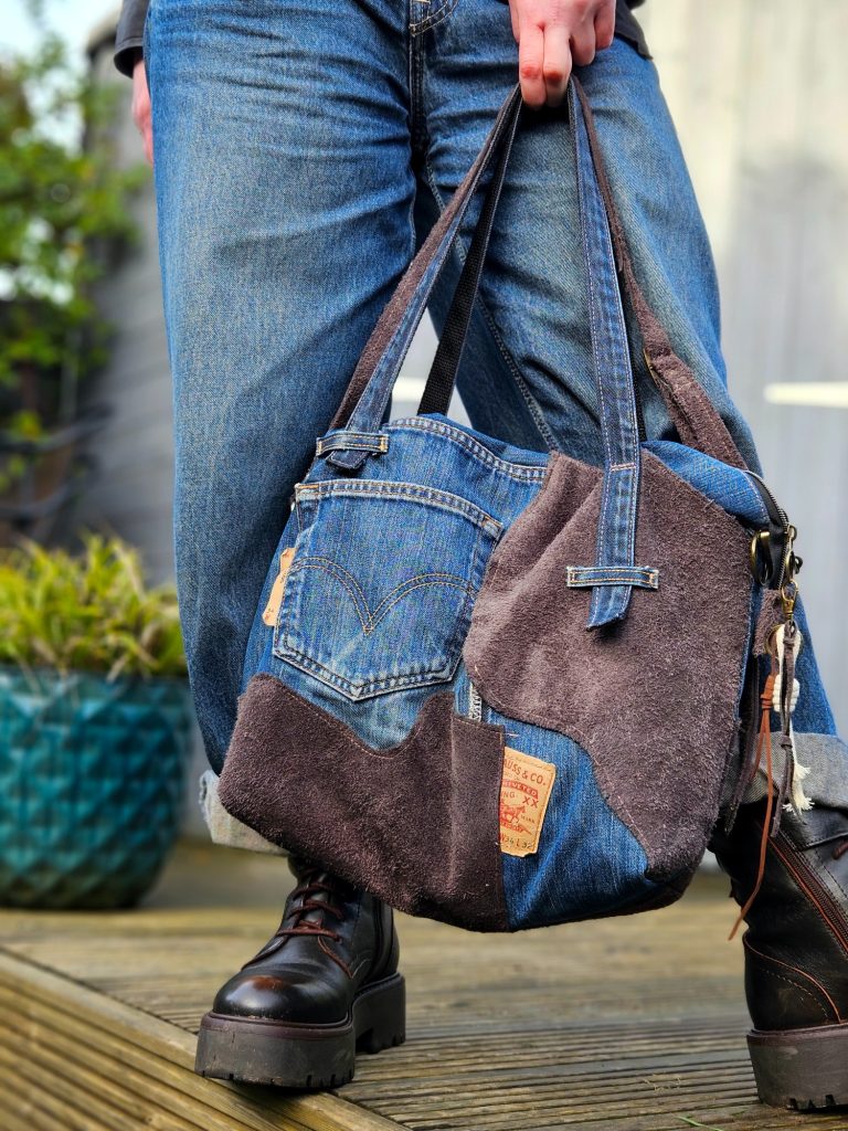 A person holding a patchwork denim handbag, wearing loose blue jeans and sturdy boots.