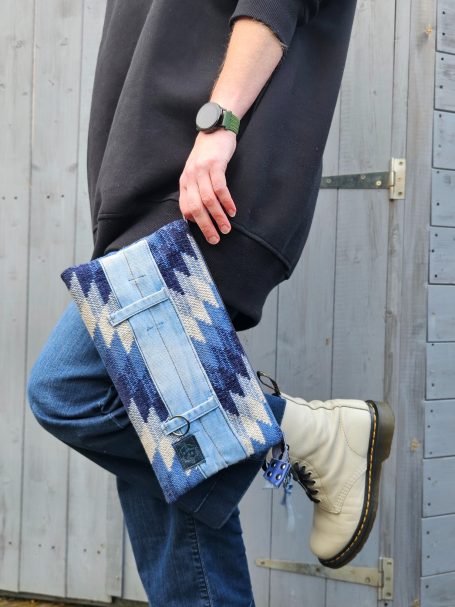 Long blue patchwork denim clutch bag carried by hand.