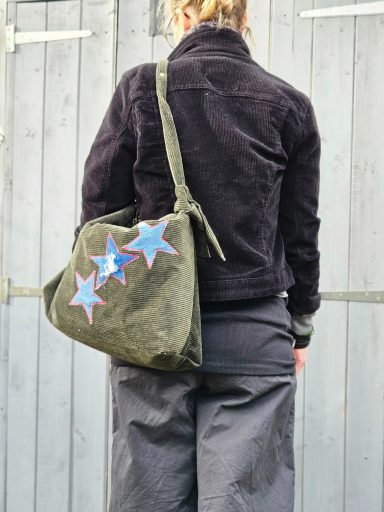 Person wearing a black jacket and grey trousers, carrying an olive green bag with blue star decorations.