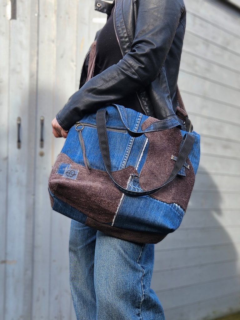 A person holding a large blue and brown fabric bag while wearing a black top and jeans.