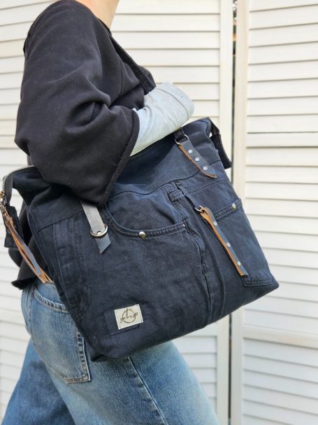 Black everyday denim tote worn on the shoulder, showing its roomy shape and useful front pocket details.