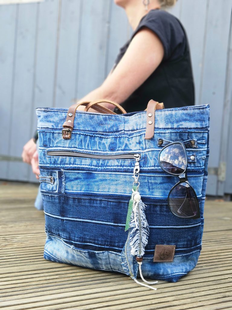 Denim Tote Bag Denim tote bag with leather handles and decorative keychain, worn by a person.