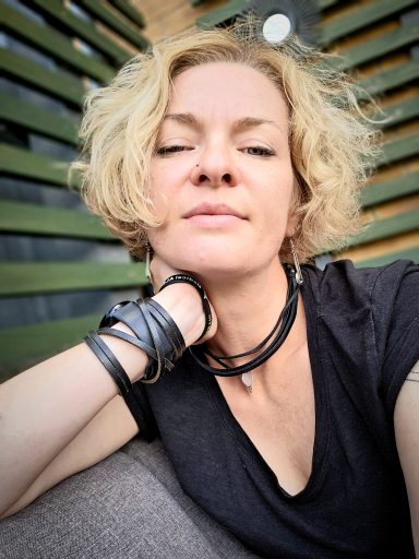 Woman with short, curly blonde hair relaxing against a backdrop of green stripes.