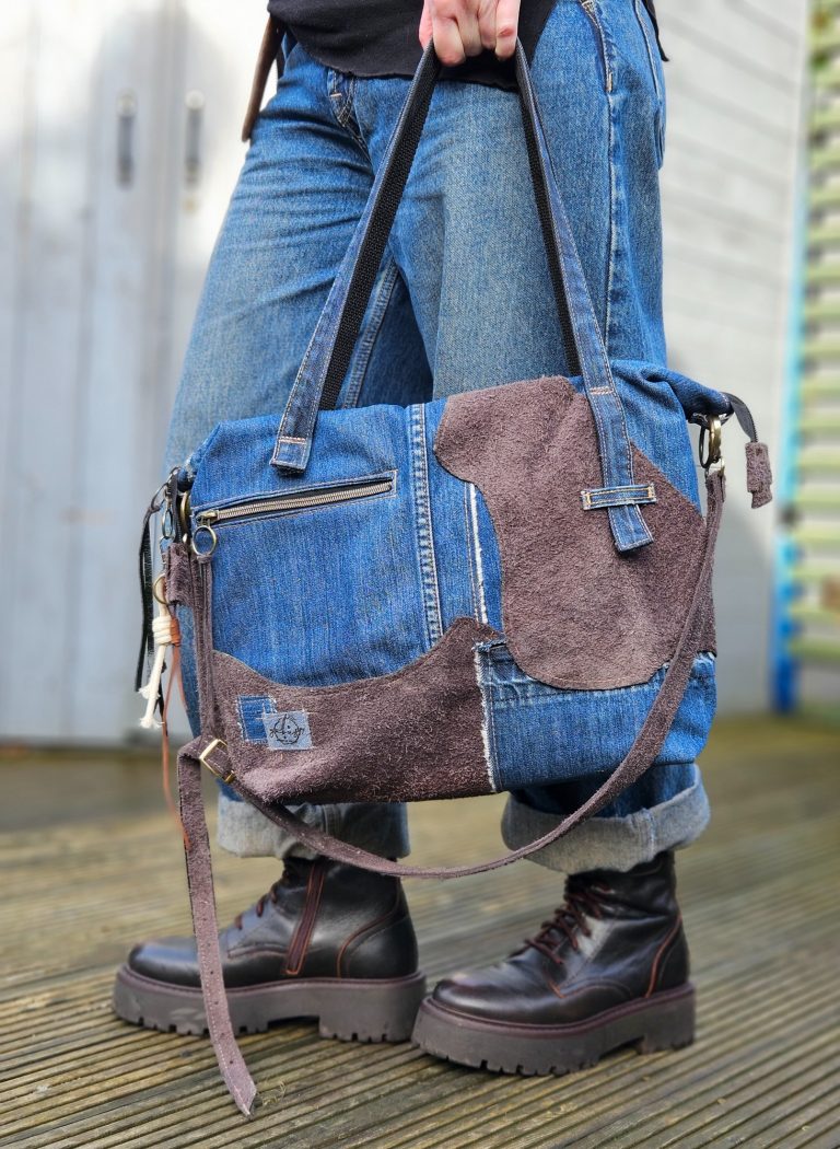 A person wearing jeans and boots, holding a stylish patchwork bag.