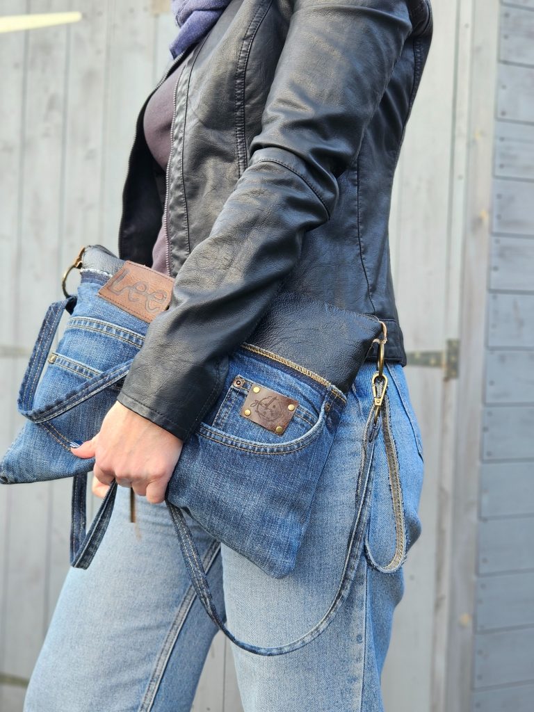 Denim Clutch A person holding two denim bags, wearing a black jacket and casual blue jeans.