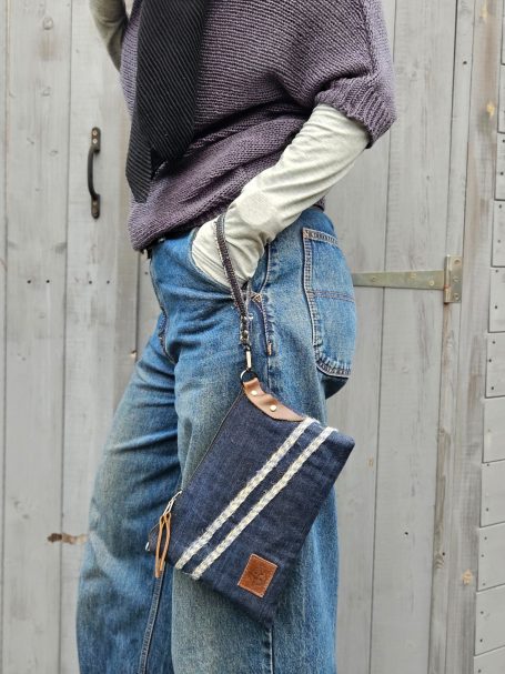 Denim clutch pouch held in hand with slim shape and wrist strap detail