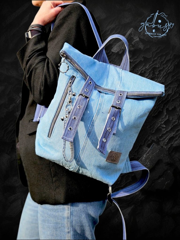 Blue denim backpack with adjustable straps and decorative stitching, worn by a person.